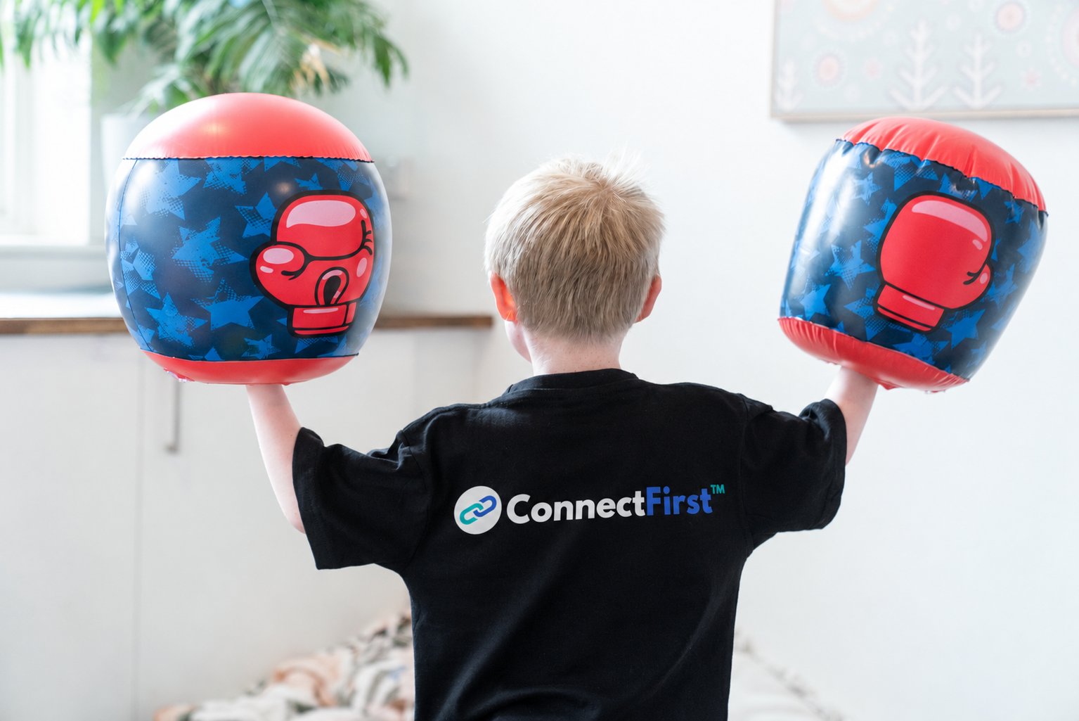 A child in a ConnectFirst t-shirt playing with inflatable boxing gloves